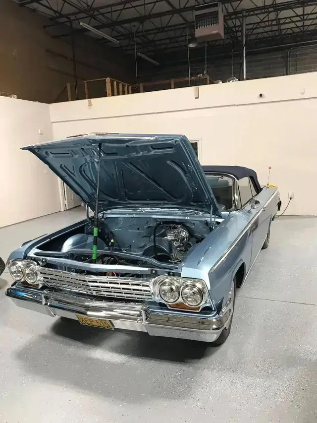 A blue classic Impala convertible in the bay with the hood up