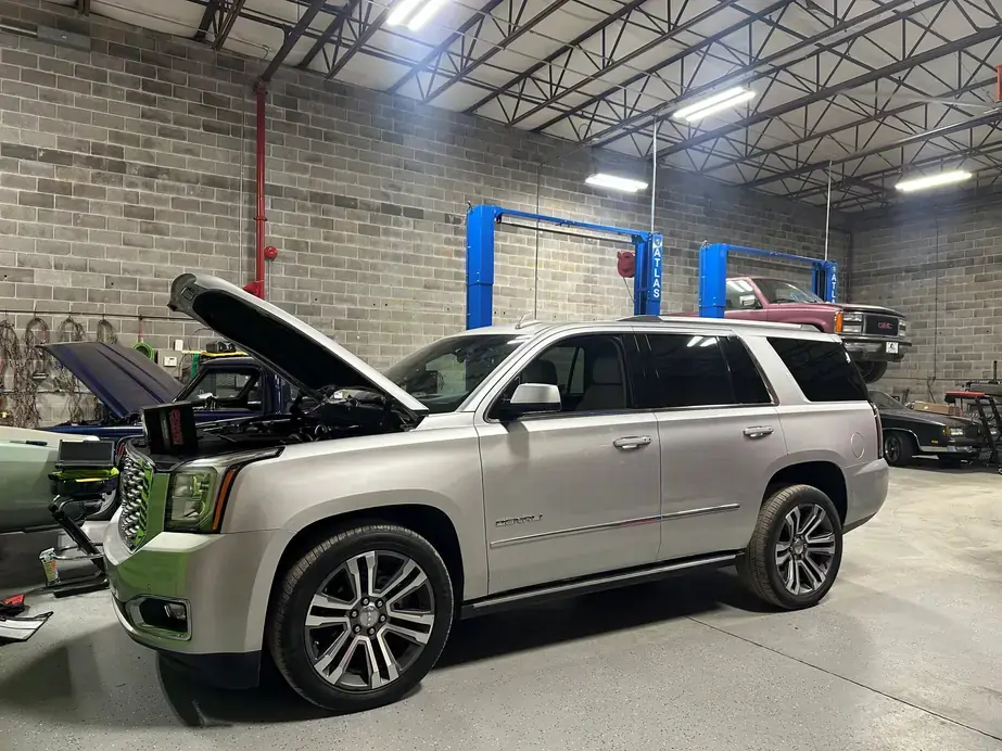 The wide shop floor with a Denali mid service, a square body GMC on the blue Atlas lift and a classic truck with its hood open