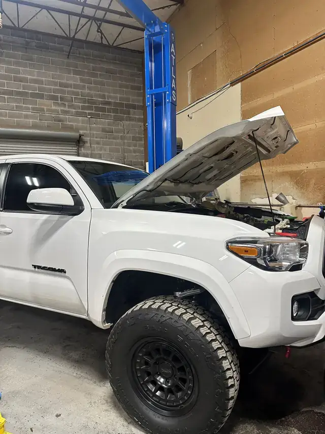 A lifted white Toyota Tacoma with the hood up on custom wheels