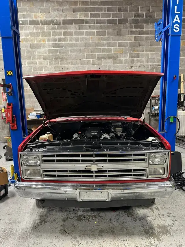 A red classic Chevrolet pickup on the lift at Lug Nutz Automotive with the hood up and a Vortec 6000 engine fitted