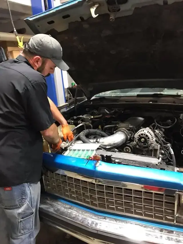 A technician working under the hood of a classic blue truck