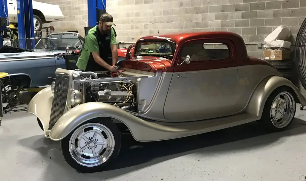 A Lug Nutz Automotive technician working on a candy red and champagne three window hot rod coupe in the shop